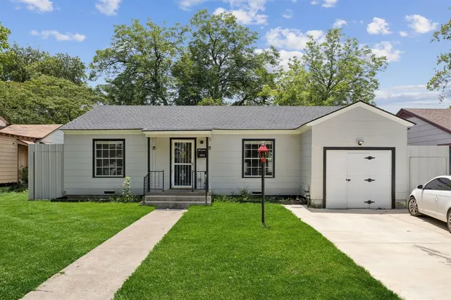 a view of a yard in front of a house with plants and large tree