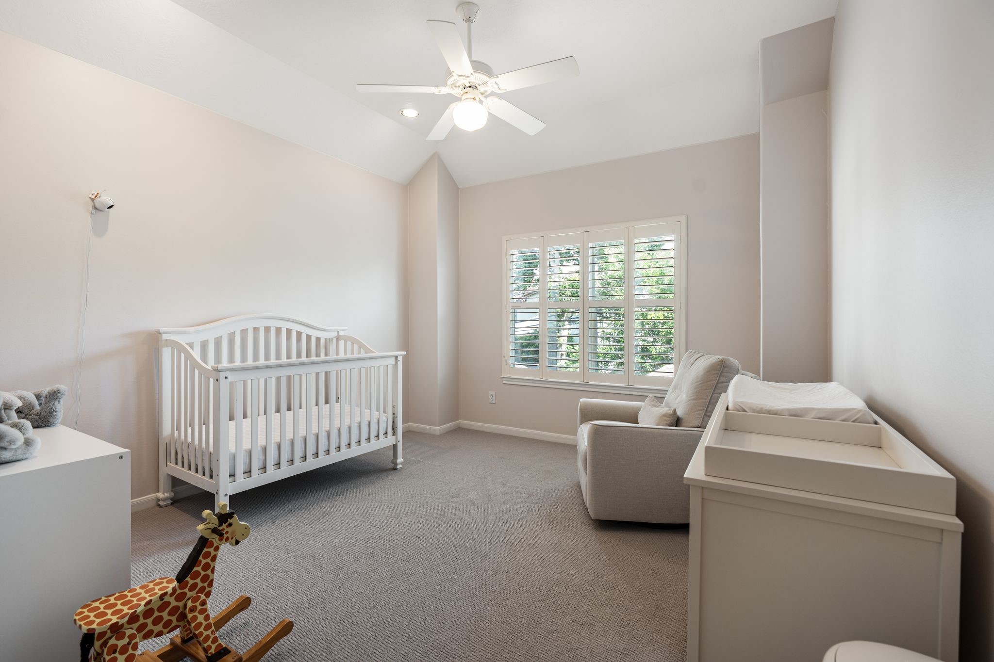 3822 Merrick Street Houston, TX 77025 - Photo 24 of 34 This upstairs bedroom features vaulted ceilings, plush carpet, a ceiling fan with light kit, and a plantation shutter window overlooking the treetops. The room is generously sized with clean neutral walls and good natural light.