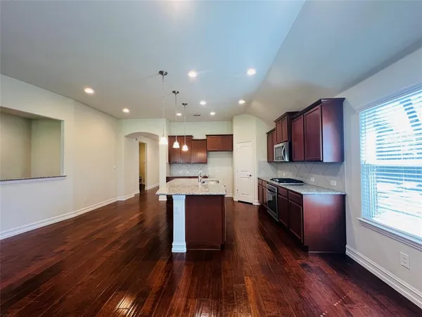 a kitchen with stainless steel appliances granite countertop wooden cabinets a stove top oven a sink and dishwasher with wooden floor