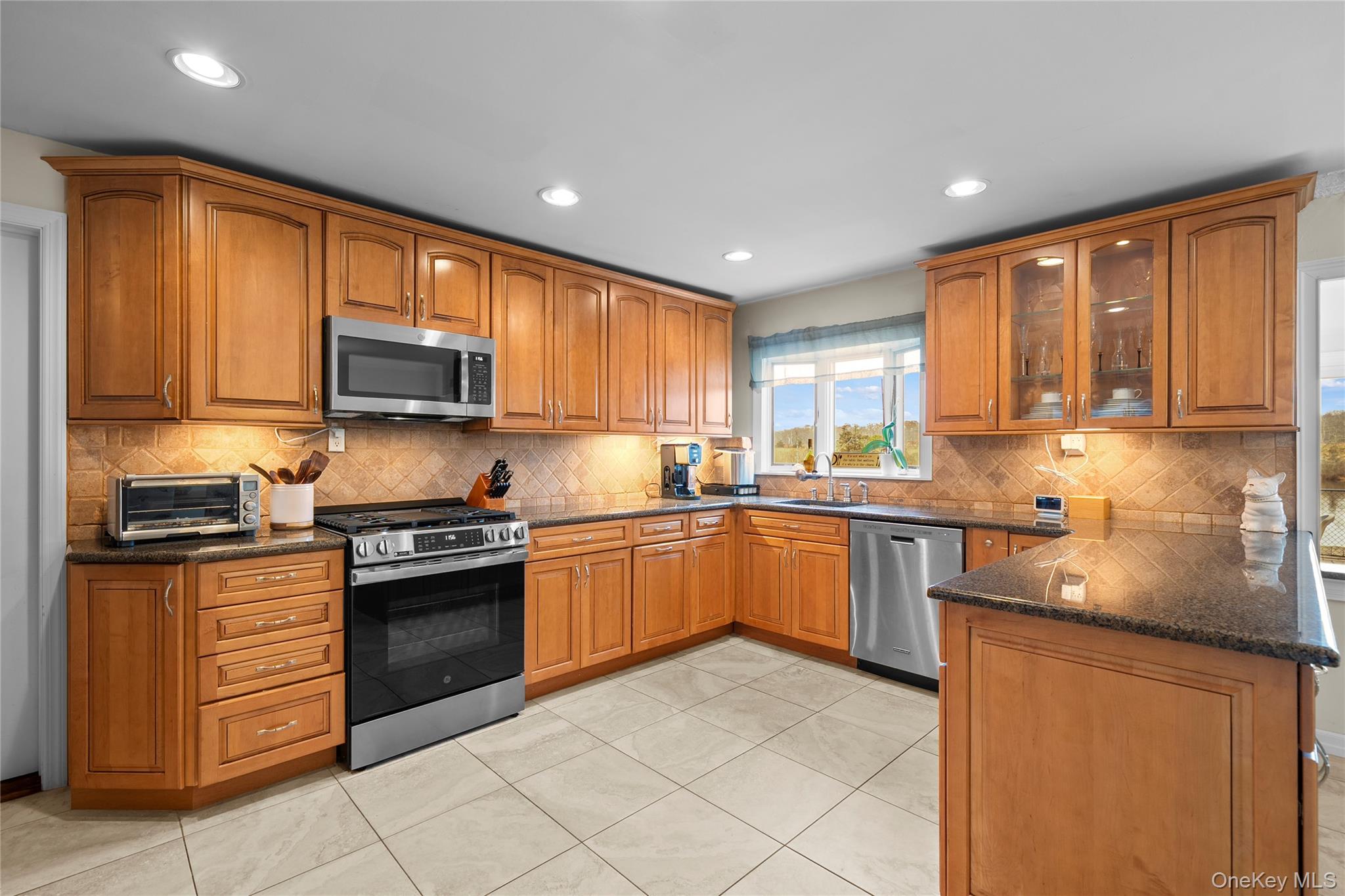 625 Edgewater Road Oakdale, NY 11769 - Photo 13 of 49 Kitchen featuring brown cabinetry, stainless steel appliances, dark stone countertops, decorative backsplash, and recessed lighting