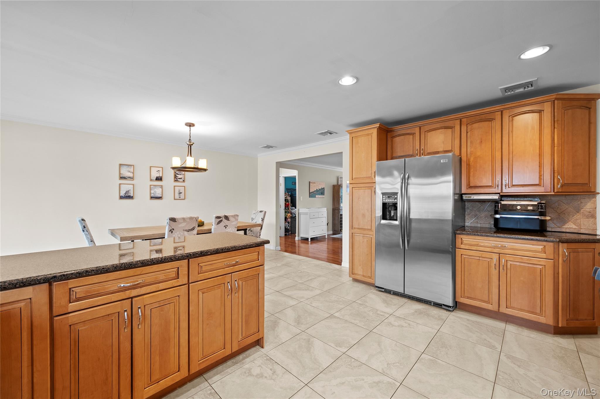 625 Edgewater Road Oakdale, NY 11769 - Photo 16 of 49 Kitchen featuring stainless steel fridge, crown molding, brown cabinetry, dark stone counters, and decorative backsplash
