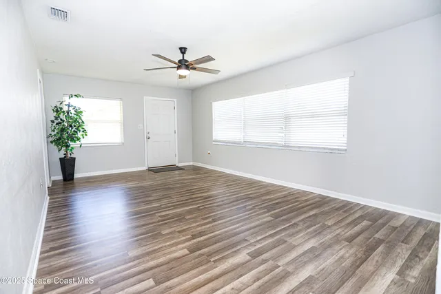 an empty room with wooden floor chandelier fan and windows