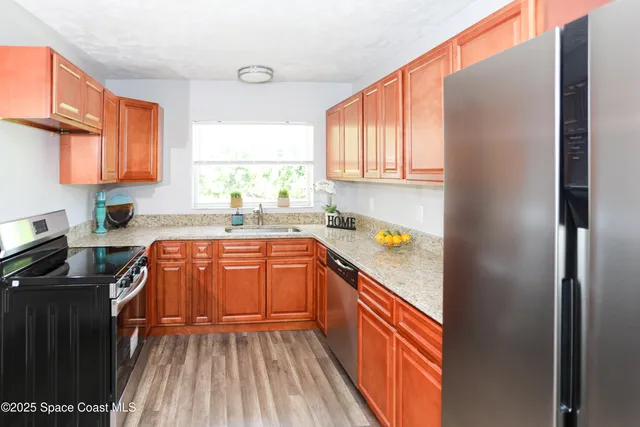 a kitchen with stainless steel appliances granite countertop a refrigerator a sink dishwasher a stove and white countertops with wooden floor