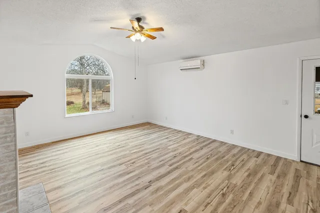 a view of an empty room with wooden floor a fireplace and a window