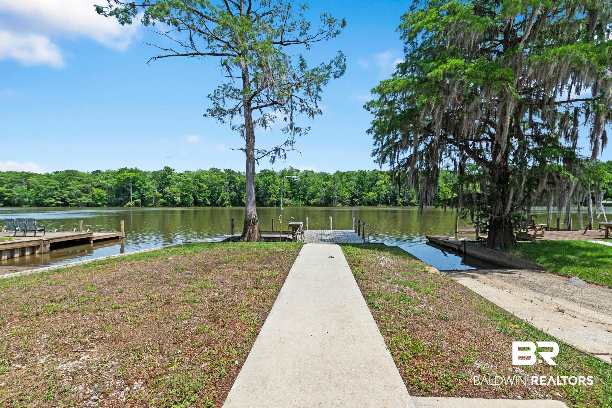 8153 Bryant's Lndg Road Stockton, AL 36579 - Photo 70 of 87 Concrete pathway leading to a waterfront area with a wooden pier, an additional wooden dock, and a boat ramp