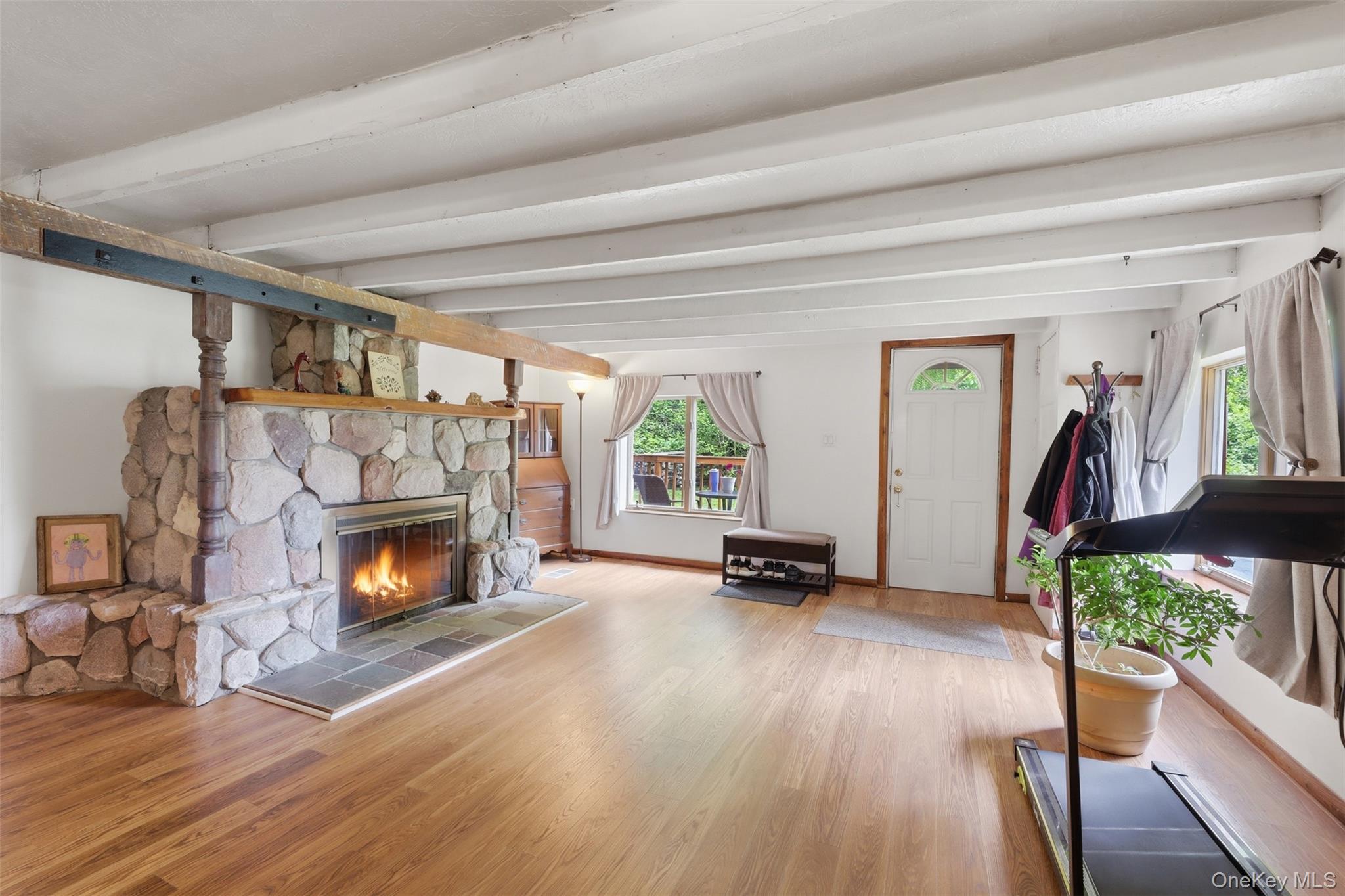 236 Hosner Mountain Road Hopewell Junction, NY 12533 - Photo 9 of 46 Living area featuring a stone fireplace with a wood mantle, wood-finish flooring, exposed white ceiling beams, and multiple windows, AI-generated flames