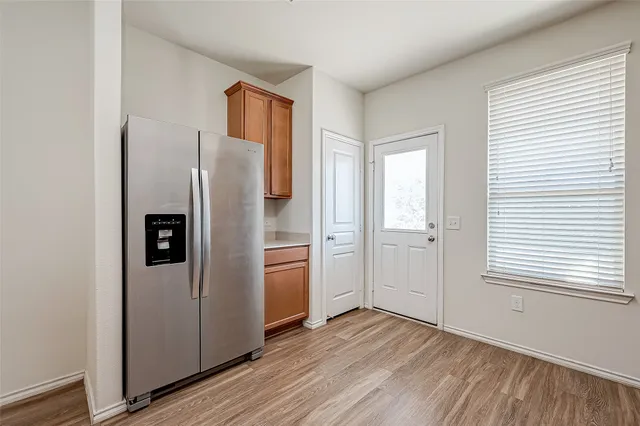 a view of a refrigerator in kitchen and an empty room with wooden floor windows
