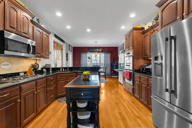 a kitchen with stainless steel appliances granite countertop a refrigerator a stove top oven a sink dishwasher and white cabinets with wooden floor