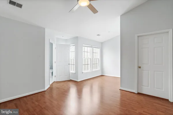 an empty room with wooden floor chandelier fan and windows