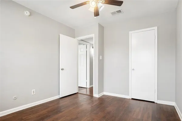 an empty room with wooden floor chandelier fan and windows