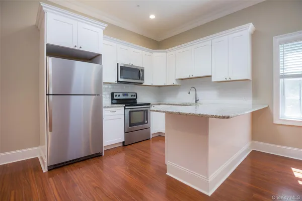 a kitchen with granite countertop a refrigerator stove a sink and white cabinets with wooden floor
