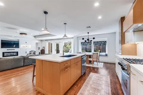 a open kitchen with stainless steel appliances granite countertop a stove top oven a sink dishwasher a dining table and chairs with wooden floor