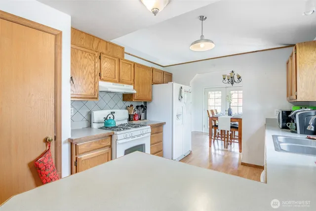 a kitchen with stainless steel appliances granite countertop a refrigerator a sink dishwasher a dining table and chairs with wooden floor