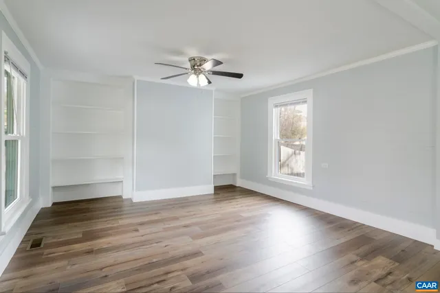an empty room with wooden floor chandelier fan and windows