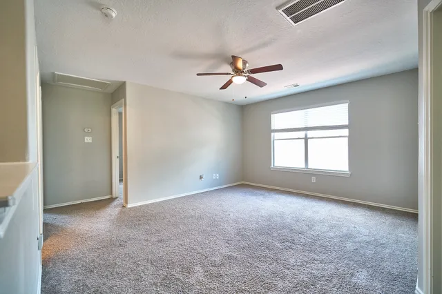 an empty room with chandelier fan and windows