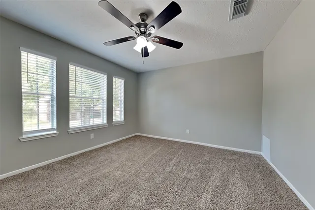 an empty room with chandelier fan and windows
