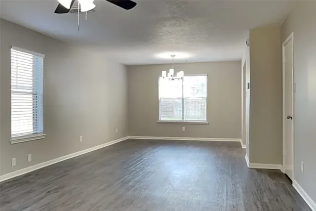 an empty room with wooden floor chandelier fan and windows