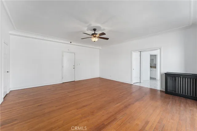 a view of an empty room with chandelier fan and wooden floor
