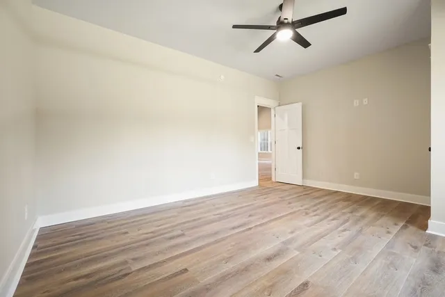an empty room with wooden floor fan and windows