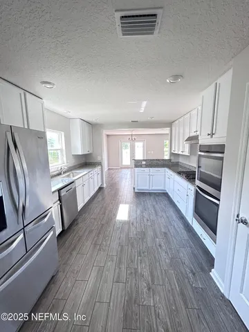 a large white kitchen with a stove a sink a window and white cabinets