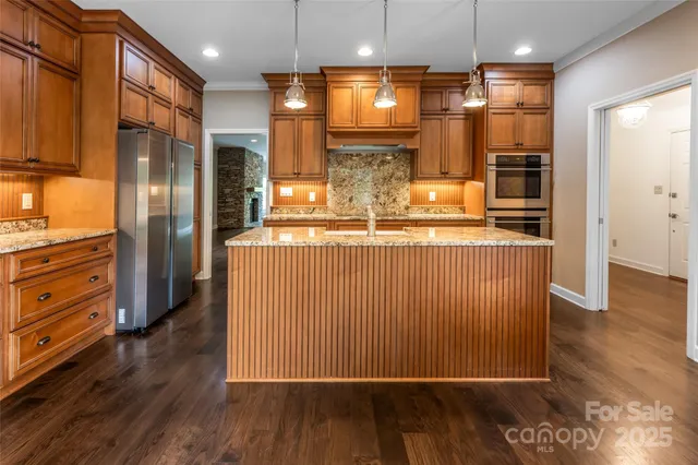 a view of a kitchen with kitchen island a refrigerator wooden floor and a view of living room