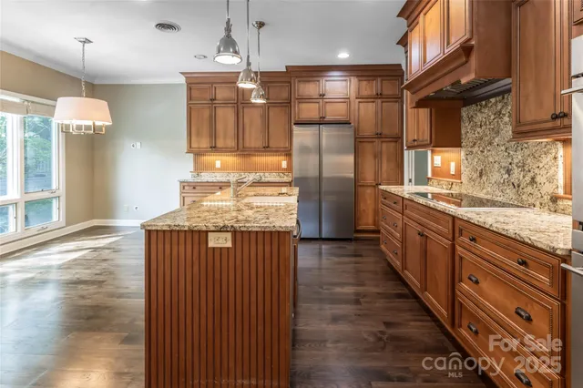 a kitchen with stainless steel appliances granite countertop a refrigerator a sink dishwasher a stove and a dining table with wooden floor