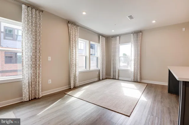 an empty room with wooden floor and windows with curtains