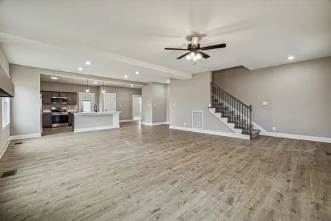 a view of an empty room with wooden floor and a ceiling fan