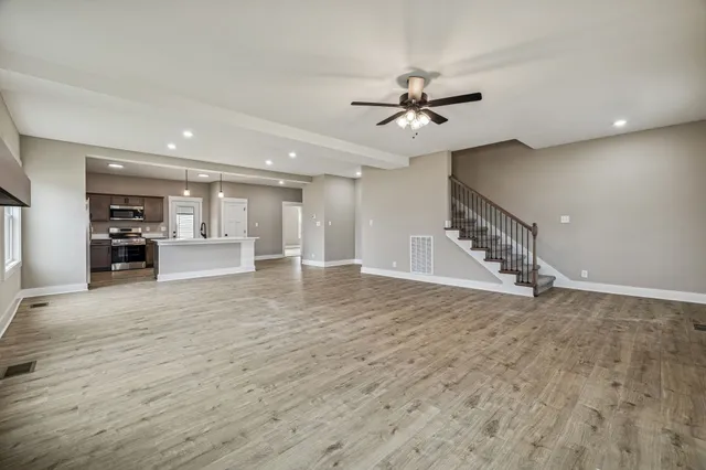 a view of an empty room with wooden floor and a ceiling fan