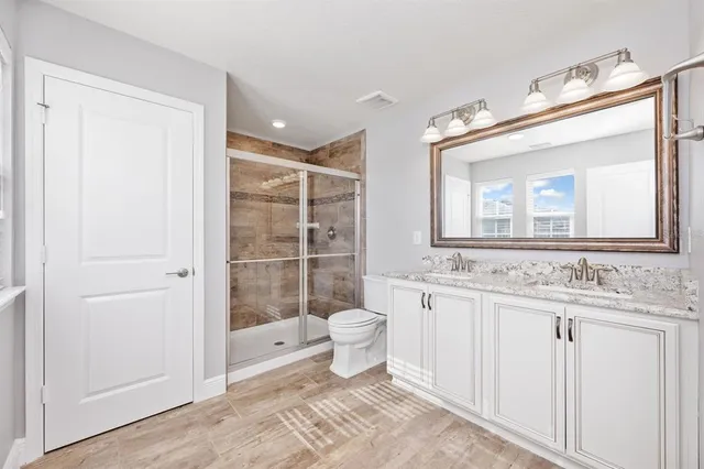 a bathroom with a granite countertop sink a toilet a mirror and shower