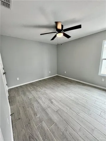 an empty room with wooden floor fan and windows