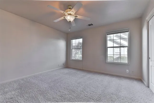 an empty room with chandelier fan and windows