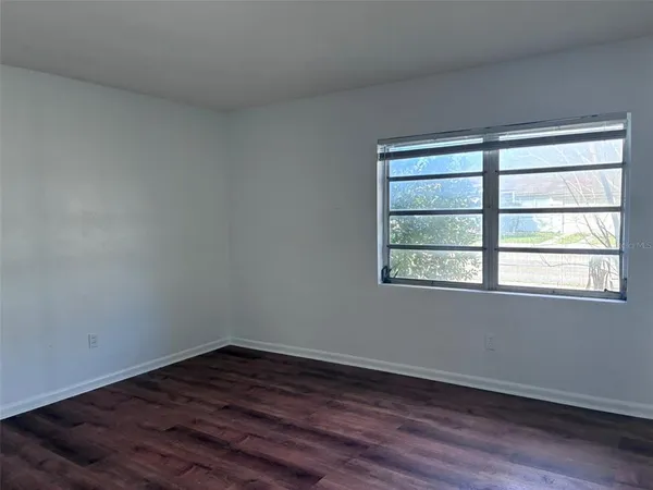a view of an empty room with wooden floor and a window