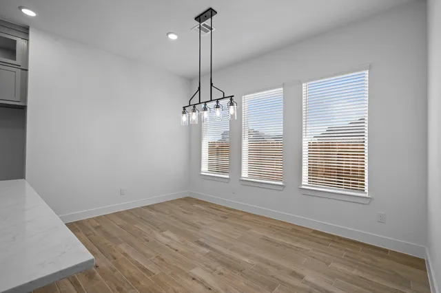 a view of an empty room with wooden floor kitchen and a window
