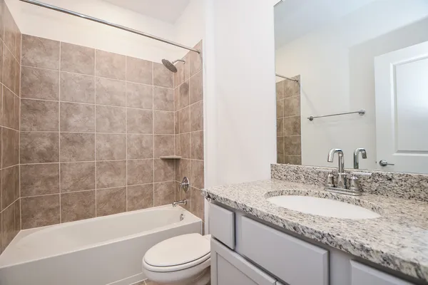 a bathroom with a granite countertop bathtub shower sink vanity and toilet