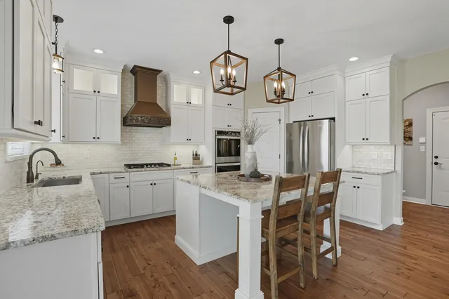 a kitchen with stainless steel appliances granite countertop a sink a stove top oven a refrigerator with white cabinets and wooden floor