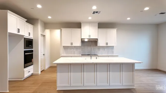 a large kitchen with stainless steel appliances kitchen island granite countertop a refrigerator a sink and white cabinets with wooden floor