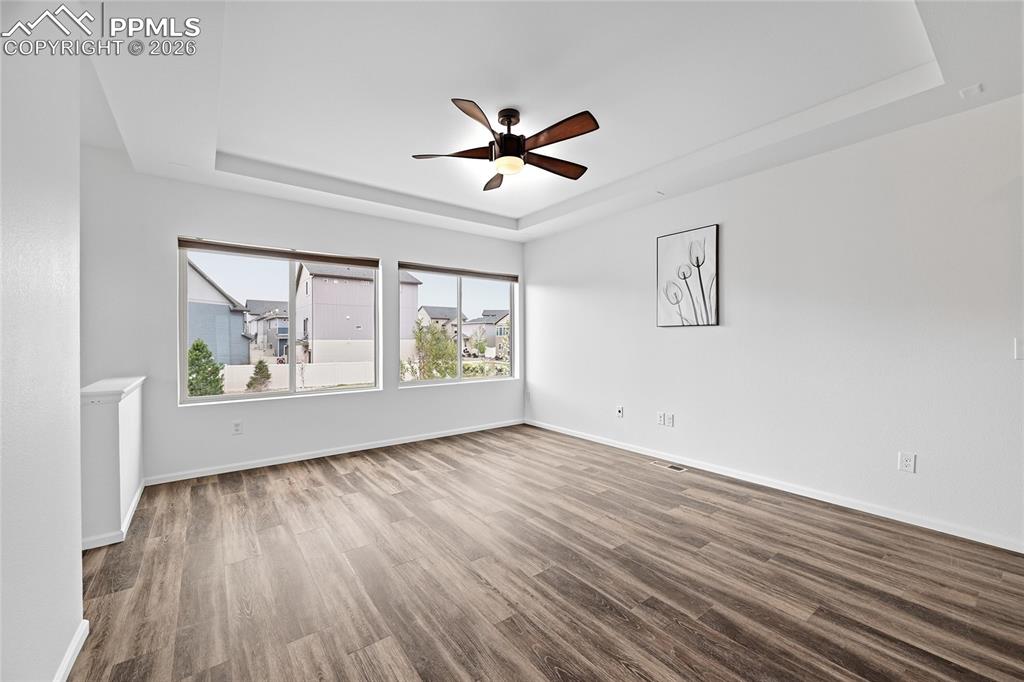 9414 Timberlake Loop Colorado Springs, CO 80927 - Photo 10 of 40 Unfurnished living room featuring two big windows, a raised ceiling, a ceiling fan, and dark luxury vinyl wood finished floors