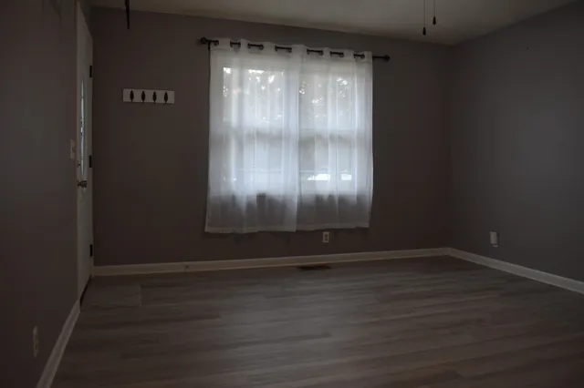 a view of an empty room with wooden floor and a window