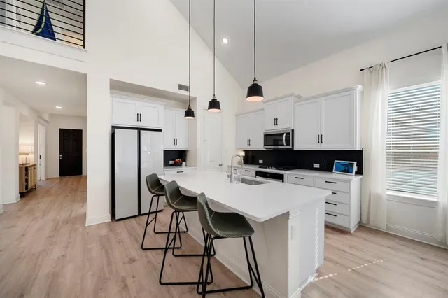 a kitchen with stainless steel appliances kitchen island a refrigerator a stove a sink a dining table and chairs with wooden floor