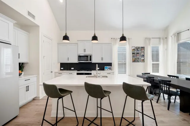 a kitchen with stainless steel appliances kitchen island granite countertop a table chairs and a white cabinets