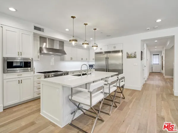 a kitchen with stainless steel appliances kitchen island a table chairs in it and white cabinets