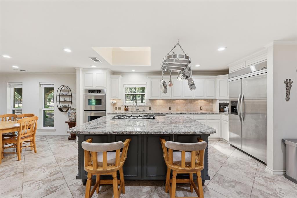 4000 Post Oak Road Flower Mound, TX 75022 - Photo 17 of 40 Main house - Kitchen featuring ornamental molding, white cabinets, light stone countertops, double ovens, appliances with stainless steel finishes, reverse osmosis under sink, and backsplash