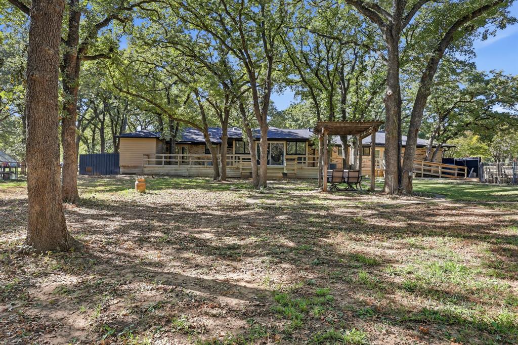 4000 Post Oak Road Flower Mound, TX 75022 - Photo 3 of 40 Rear view of main house with a wooden deck and pergola, pool is to the right and greenhouse is to the left