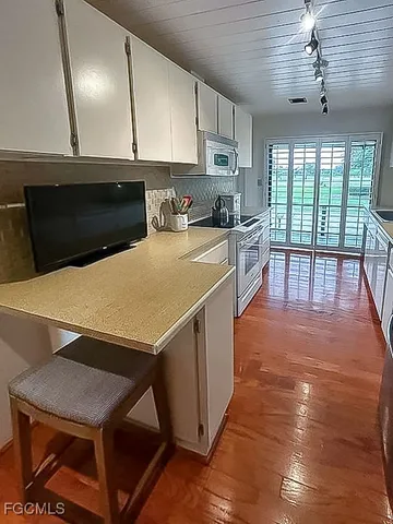 a kitchen with stainless steel appliances a stove a refrigerator a sink and white cabinets with wooden floor