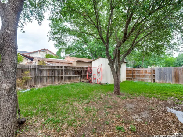 a view of backyard with large trees and wooden fence