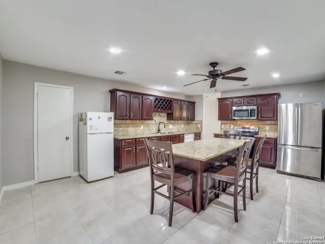 a kitchen with stainless steel appliances kitchen island granite countertop a table chairs and a refrigerator