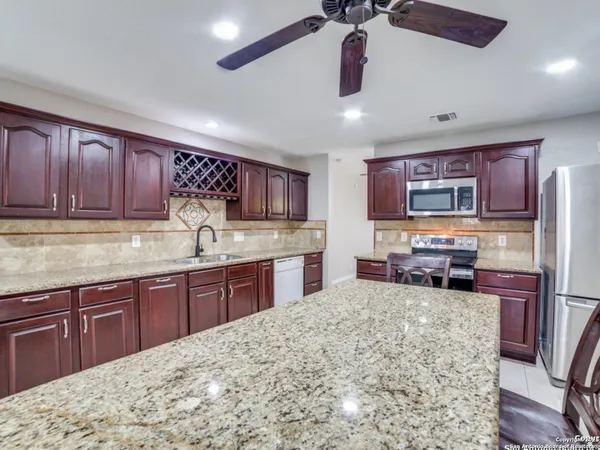 a kitchen with stainless steel appliances granite countertop wooden cabinets a sink dishwasher a stove and a refrigerator with wooden floor