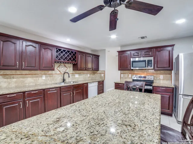 a kitchen with stainless steel appliances granite countertop wooden cabinets a sink dishwasher a stove and a refrigerator with wooden floor