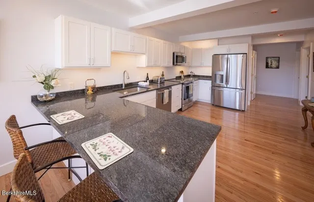 a kitchen with stainless steel appliances granite countertop a refrigerator a stove a sink a dining table and chairs with wooden floor